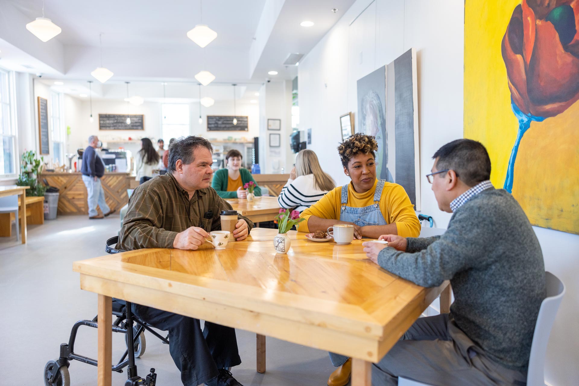 Three people, one in a wheelchair, having a conversation in a cozy living room setting with artwork on the wall.
