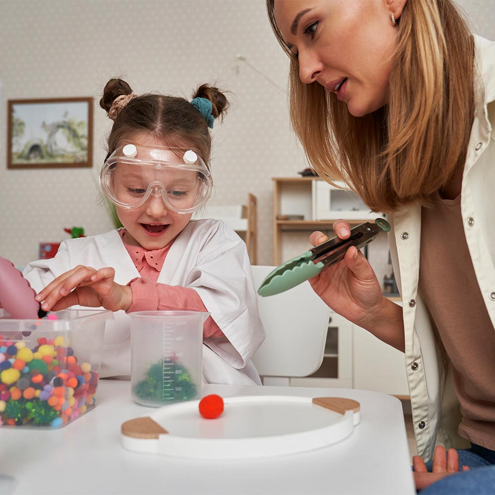 A young girl with Down syndrome and an adult conducting a science experiment with colorful liquids in a classroom.